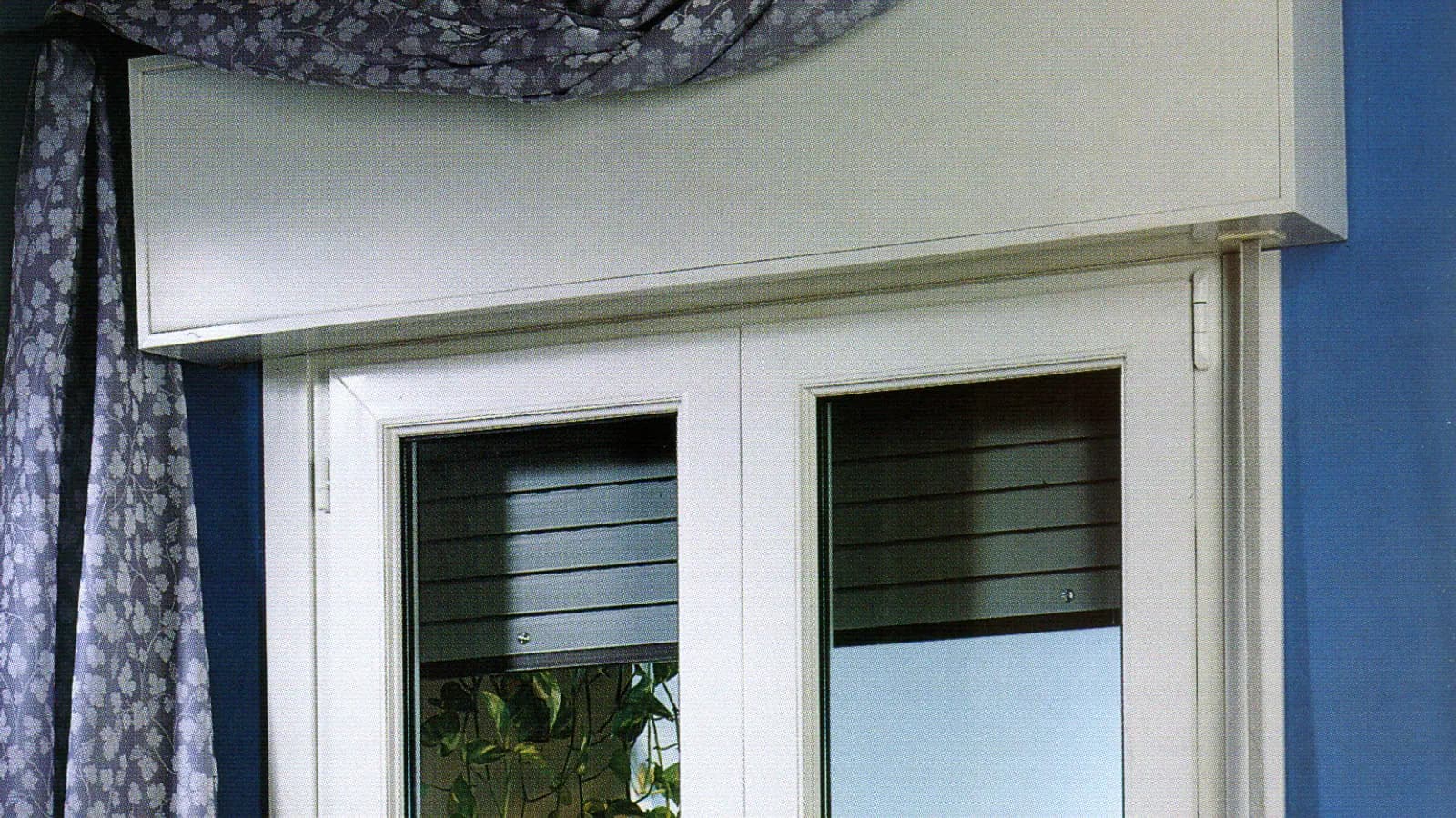 Ventana blanca de dos hojas vista desde dentro, con el cajón de persiana a la vista sobre el marco