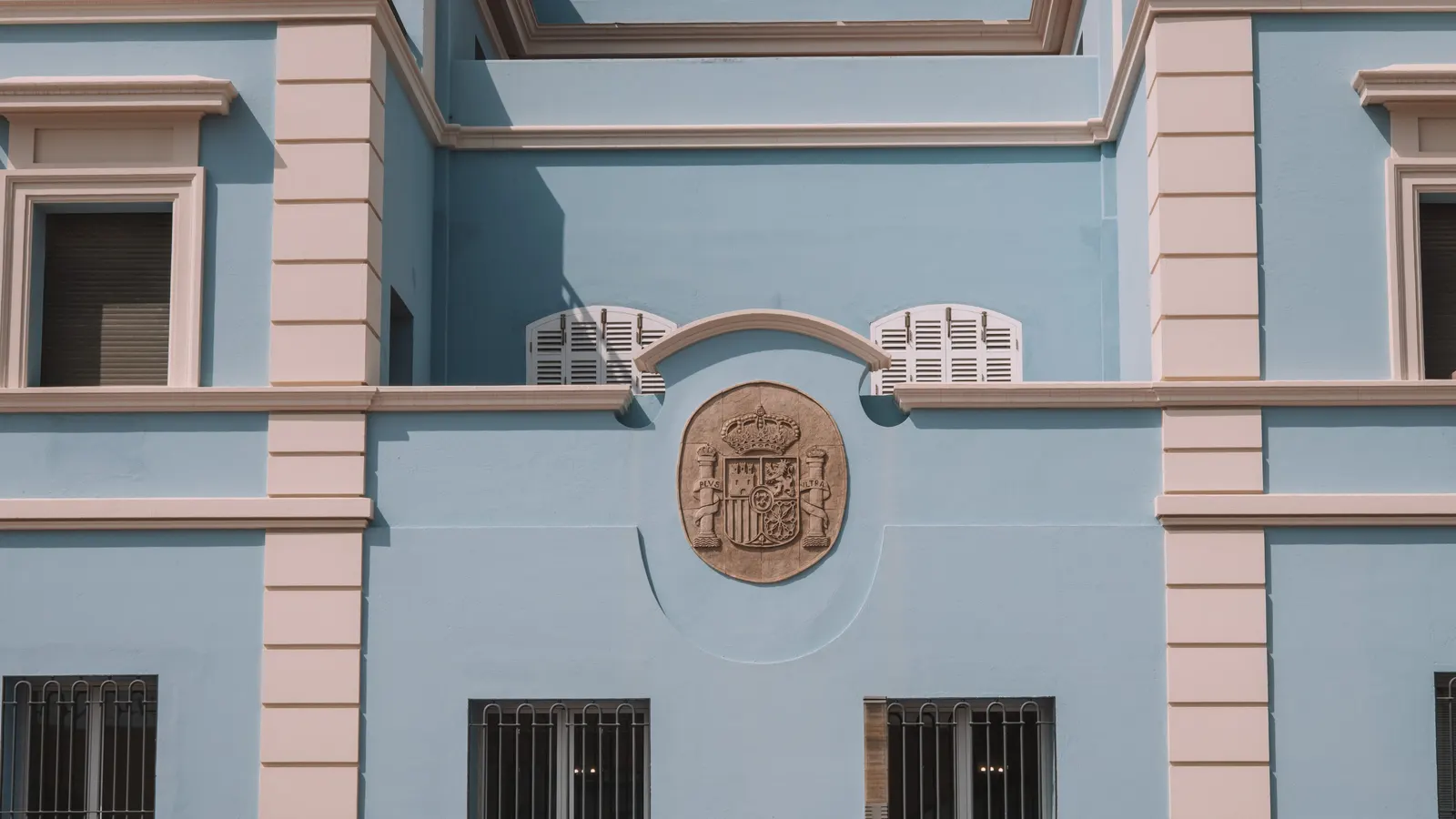 Fachada de piedra de un edificio administrativo con un escudo labrado sobre la portada y ventanas de arco en la planta principal